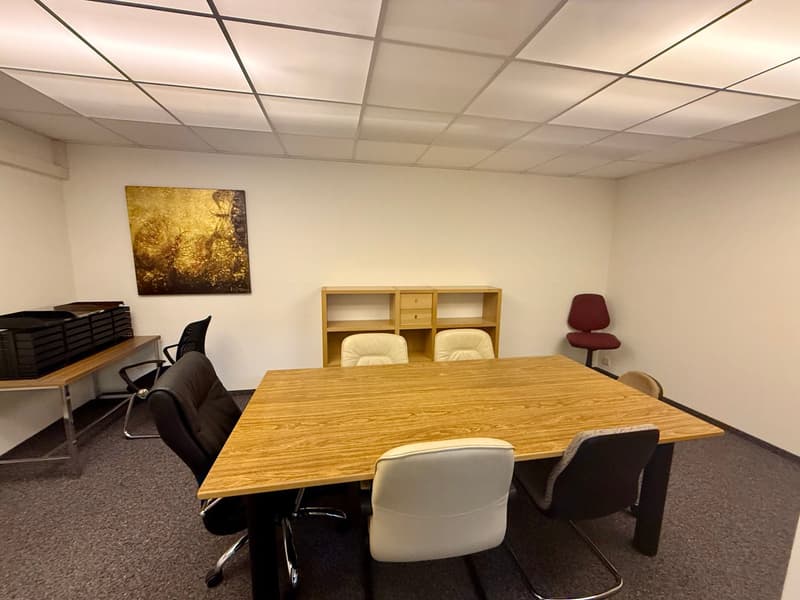 Empty office with a large wooden table, several chairs, and a cabinet. The walls are white, and there is a framed painting on one of the walls.