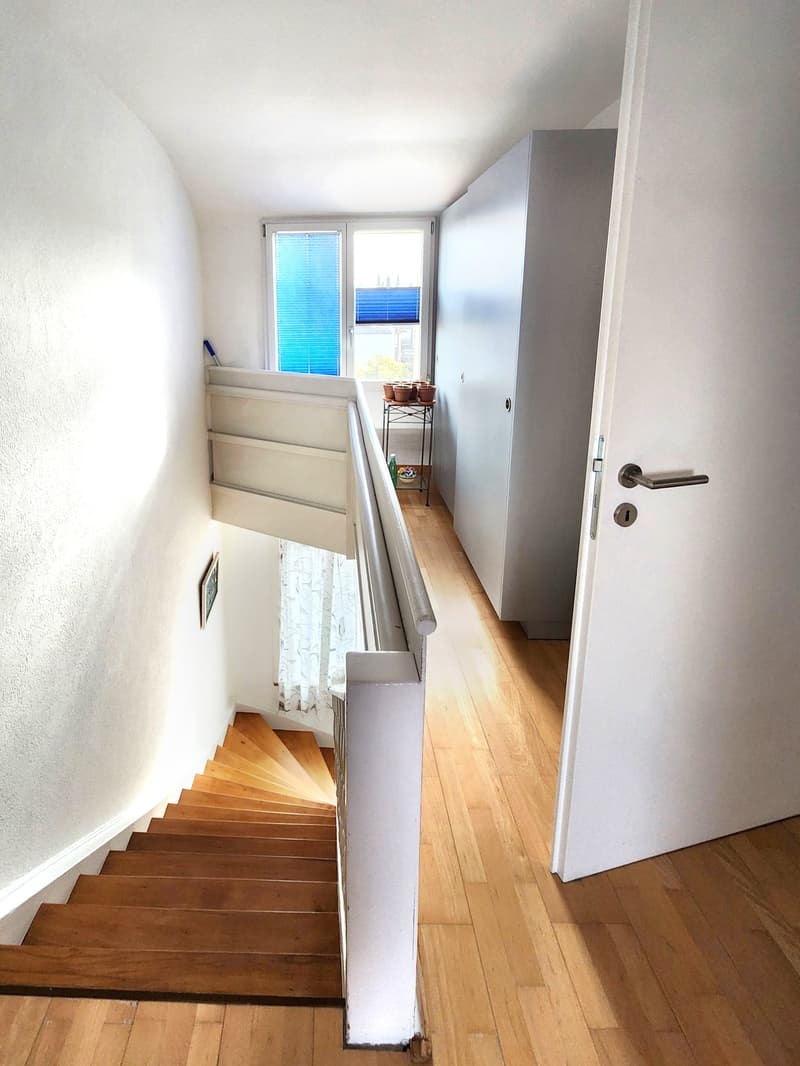 wooden stairs, white walls, wooden floor, white railing, window with blue blinds, white door, picture frame, small table with potted plants