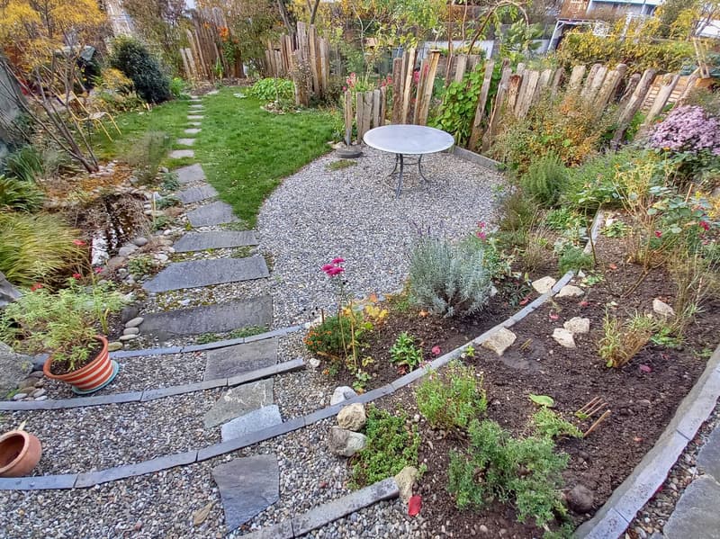 A garden with a gravel pathway, a table, and a variety of plants and flowers.