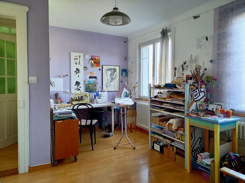 A room with a desk, chair, sewing machine, shelves, and various art supplies.