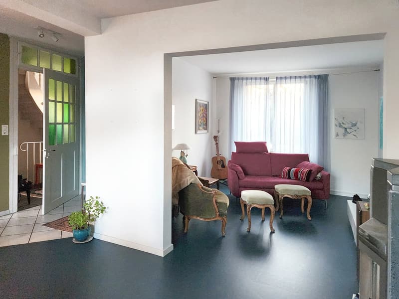 living room with white walls, black floor, red sofa, two stools, guitar, lamp, two paintings, potted plant