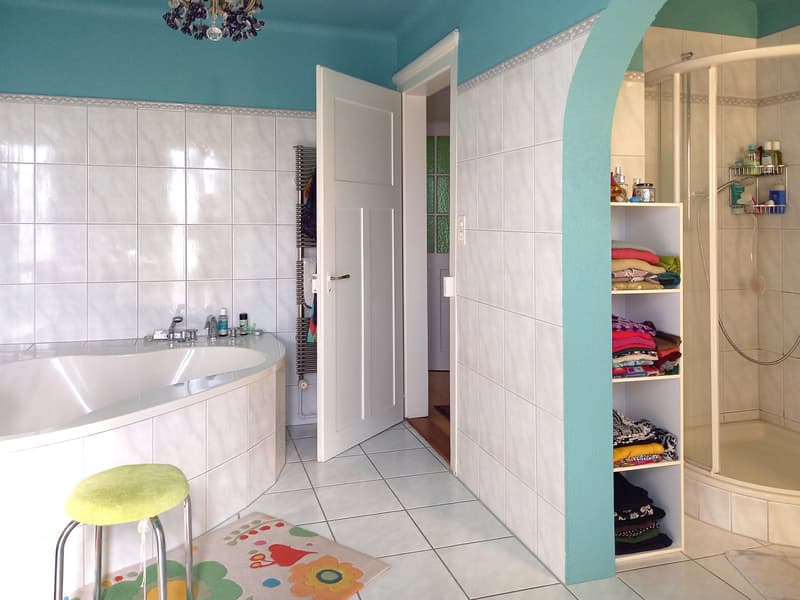 Bathroom with bathtub, shower, shelves, stool, and tiled floor.