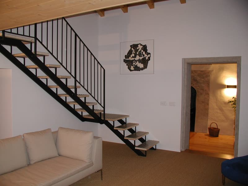 modern living room with white couch, black staircase, white walls, wooden floor