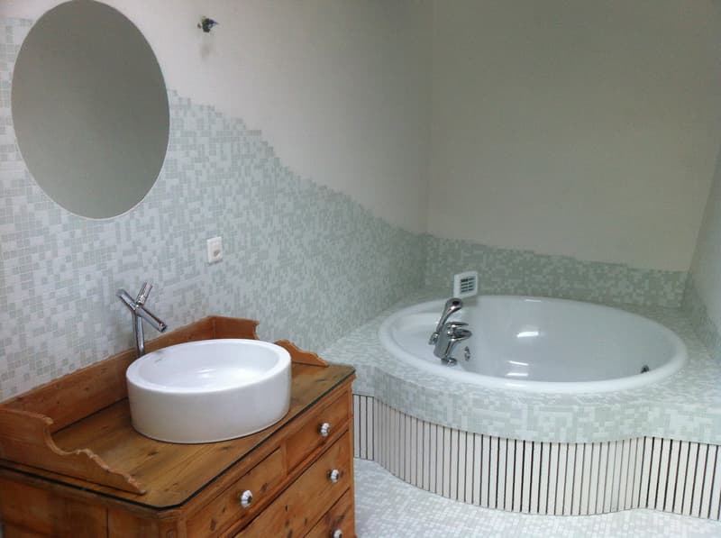 Bathroom with a wooden cabinet, a round mirror, a white sink, a round bathtub, and tiled walls.
