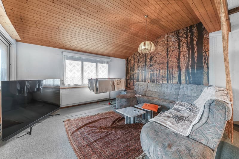 large TV, L-shaped sofa, side tables, ottoman, area rug, hanging lamp, clothes drying rack, sliding glass door