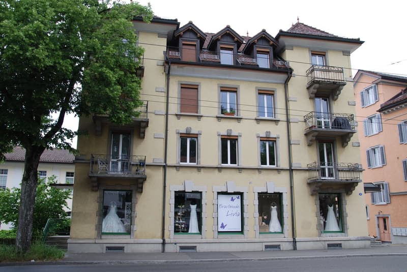 Three-story building, multiple balconies, windows with shutters, wedding dress shop on ground floor