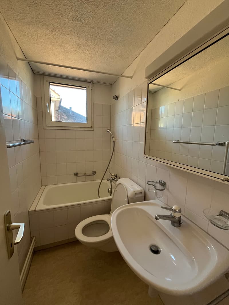 Modern bathroom with bathtub, toilet, sink, mirror, and window