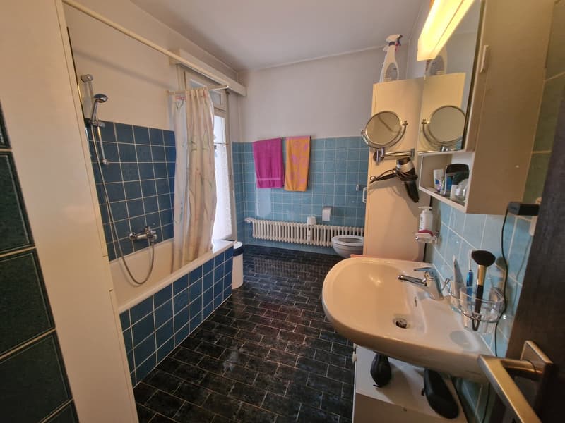Bathroom with blue tiles, white sink, shower, toilet, and towel rack.
