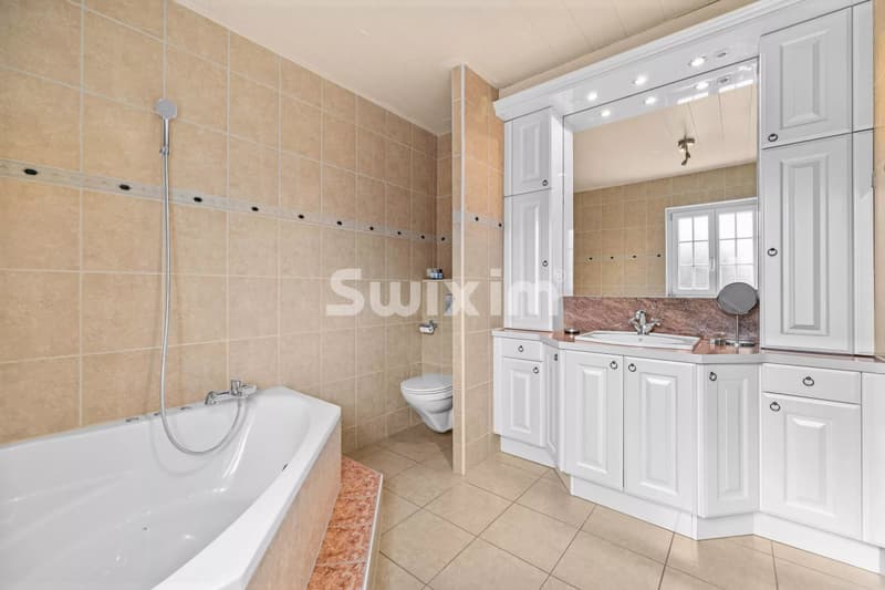 Salle de bains spacieuse avec baignoire et grand miroir intégré.