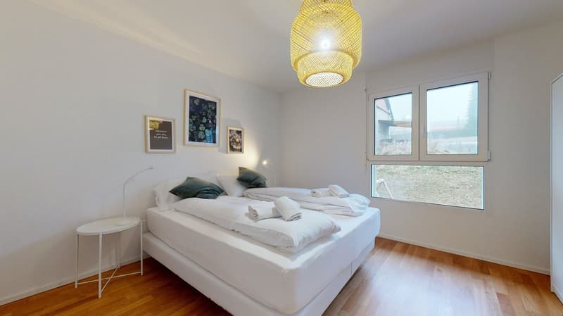white walls, wooden floor, double bed, white bedding, side table, lamp, framed pictures, large window