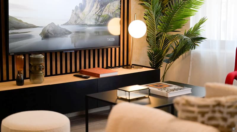 Modern living room with a large TV displaying a scenic landscape, wooden and black furniture, decorative plants, and lighting fixtures.