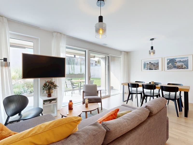 Open layout with a dining area, a living area with sofa and TV, a window leading to a terrace, and a light-filled space with ceiling lamps