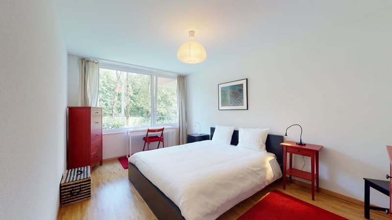 white walls, wood floor, double bed, red chair, desk, window, lamp