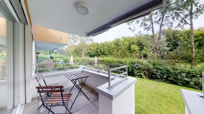 Balcony with metal railing, wooden chairs, small table, grass and plants