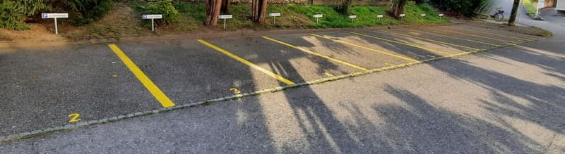A paved parking lot with several numbered parking spaces and small white signs