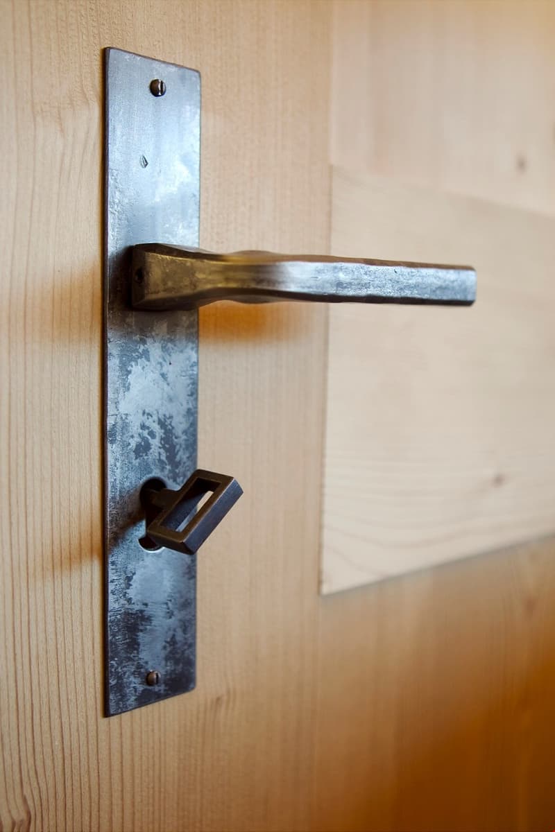 Sleek, square, rustic metal door handle with visible screws, mounted on a wooden surface