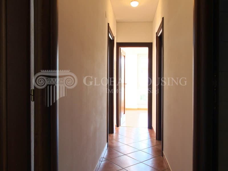 Empty corridor with tiled floor, ceiling light, open door at the end