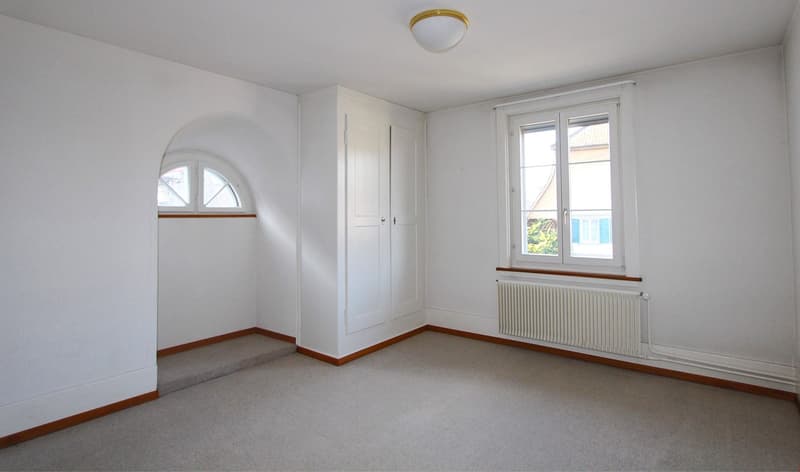 empty room, white walls, white ceiling, arched window, white radiator, white door, carpeted floor