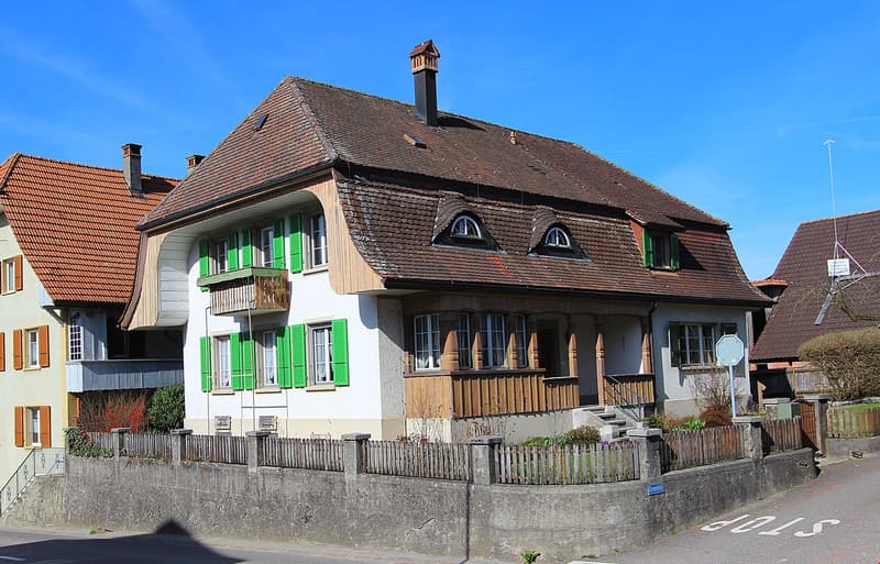 2 story house, brown roof, green shutters, wooden balcony, chimney, concrete wall, wooden fence