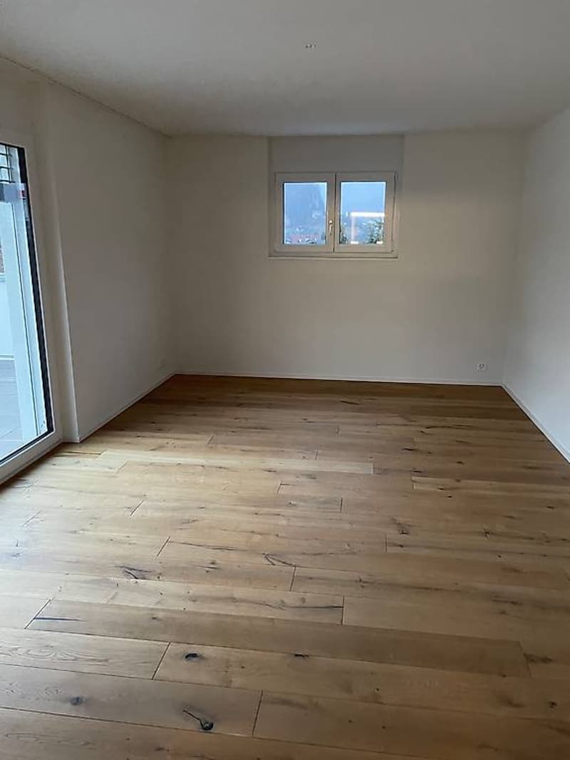 Empty room, wooden floor, white walls, sliding glass door leading to balcony, double window