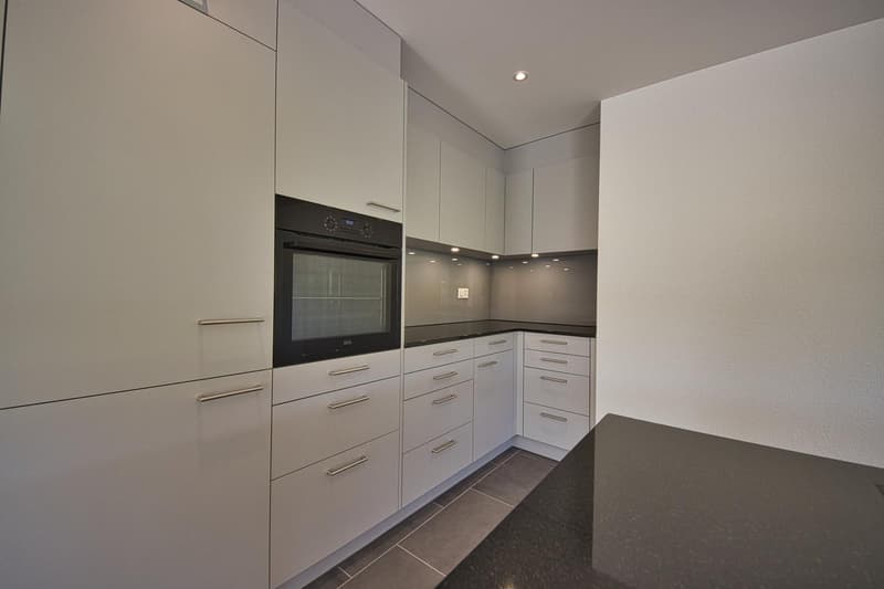Modern kitchen with sleek white cabinetry, integrated oven and dishwasher, granite countertop, tiled flooring, recessed lighting