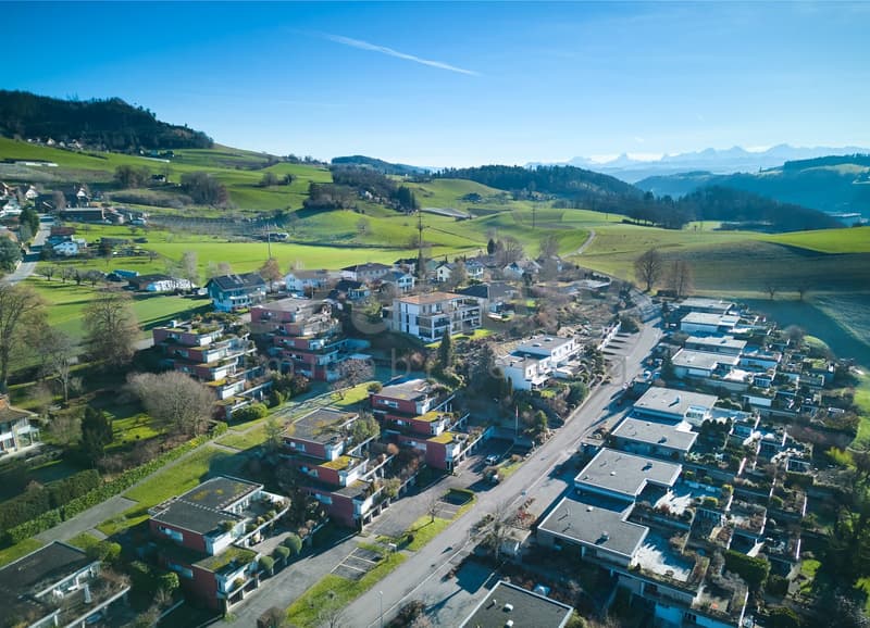 Aerial view of residential neighborhood in a valley, houses built into hillside, green fields and mountains in background.