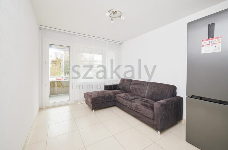 modern living room with white walls, white tile flooring, a large L-shaped sofa, a glass door leading to a balcony, and a modern refrigerator