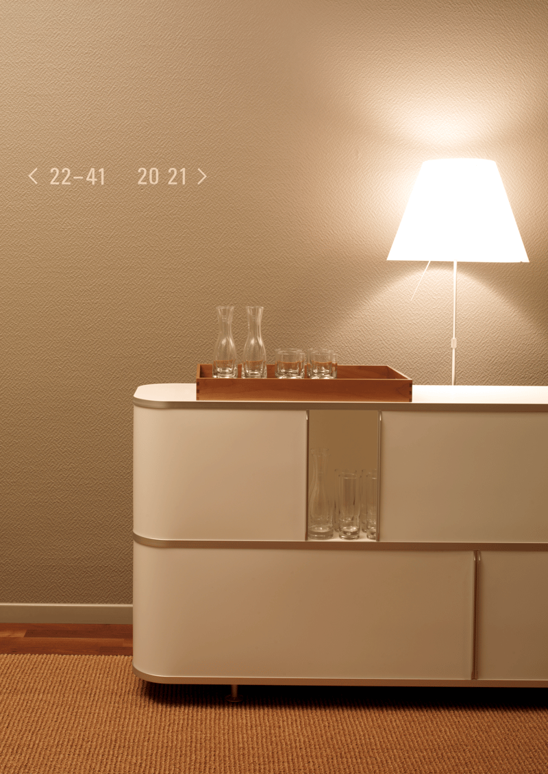 A white cabinet with a wooden tray and glass items, a white lamp on top, on a beige carpet on a wooden floor