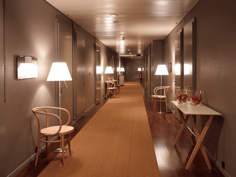 Empty hallway with beige carpeting, modern lamps, and minimalistic furniture.