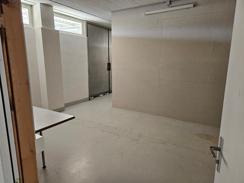 Empty room with white walls and floor, table, metal door, light fixtures