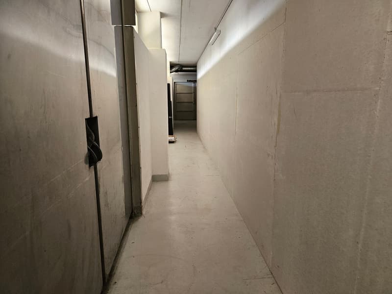 A long hallway with two sets of doors, concrete walls, and a tiled floor.