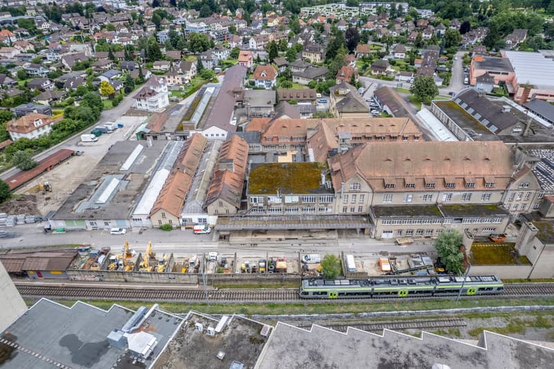 Aerial view of a town with multiple buildings, some under construction, vehicles, and a railway track with a train