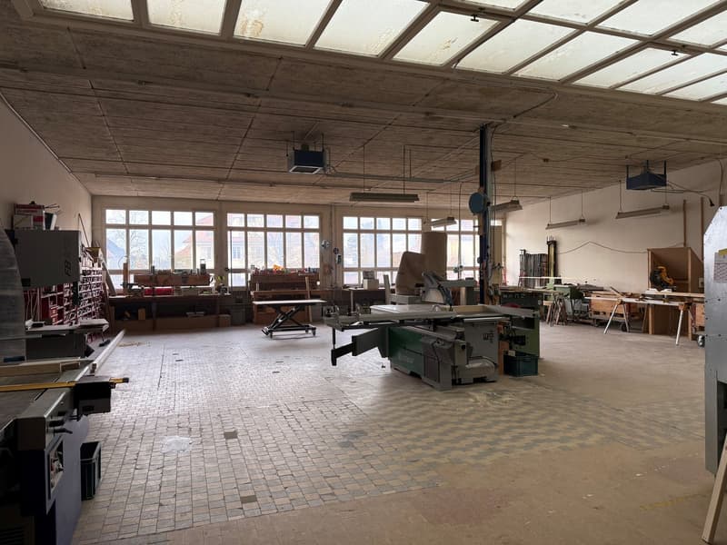 large open space with brick flooring, industrial equipment, large windows, ceiling lamps