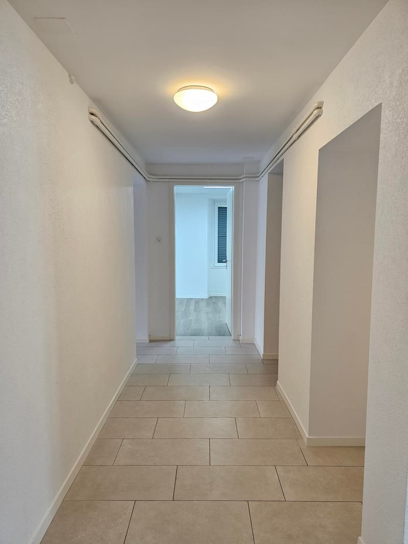 Empty hallway with tiled floor, white walls, and a ceiling light