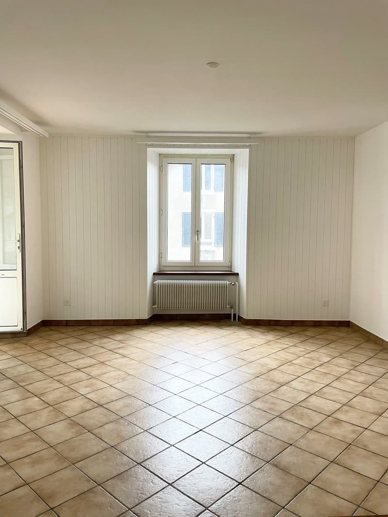 Empty room with tiled floor, white walls, open window, radiator