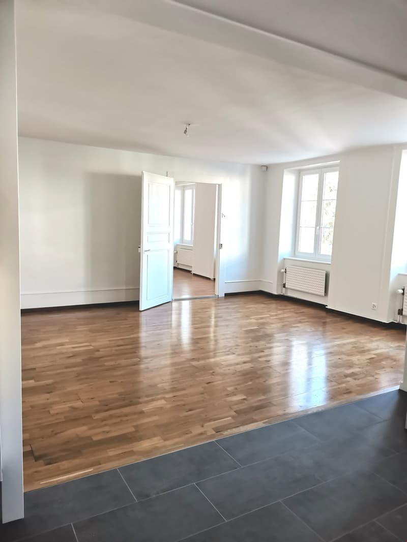 Empty room with wooden floor, white walls, two doors, and windows with white frames