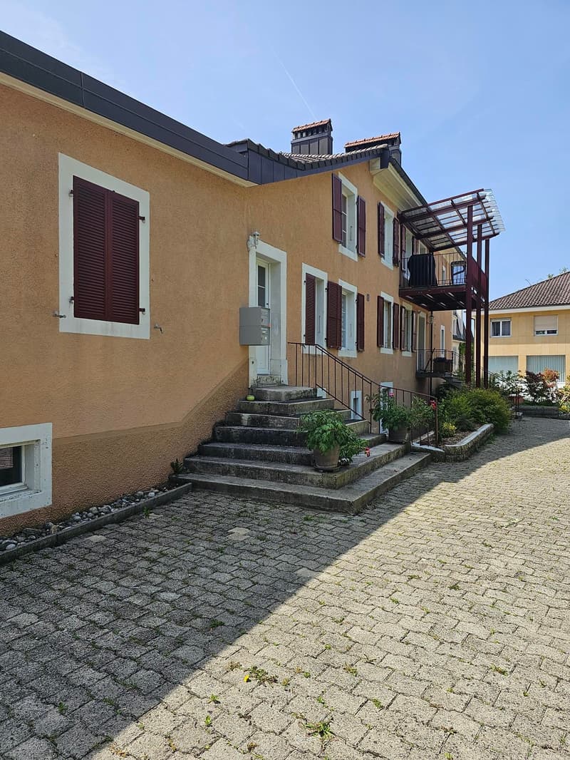 2 story house, beige exterior, brown shutters, brick driveway, stairs leading to entrance, balcony