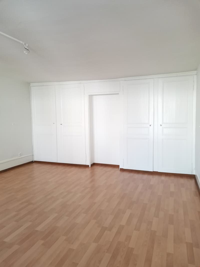 Empty room with wooden floor, white walls, built-in wardrobes, and a door.