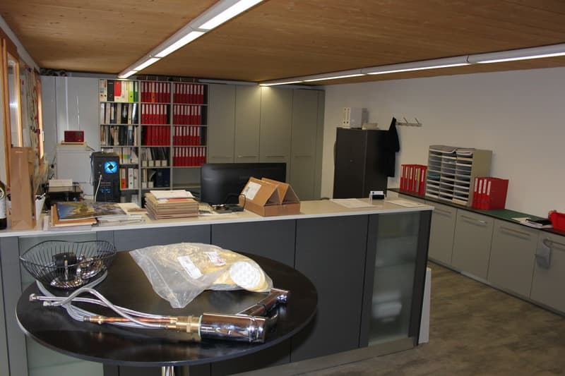 office room with monitor, file cabinets, shelf with red folders, desk, chairs