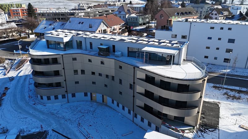Multistory building with balconies and solar panels on the roof.