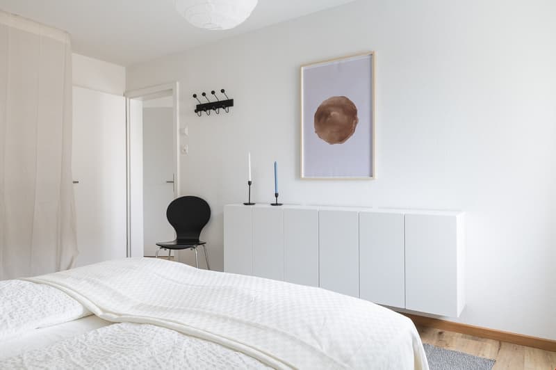 bedroom, white walls, white bed with bedding, white cabinets, black chair, white curtains
