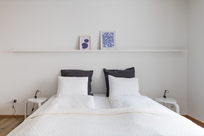 minimalist room with double bed, white bedding, black cushions, bedside tables, and wall art