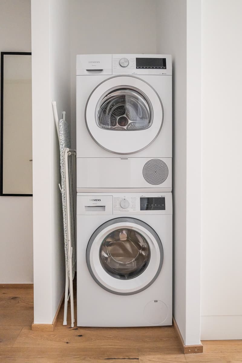 Stacked Siemens washing machine and dryer, wooden floor, white walls