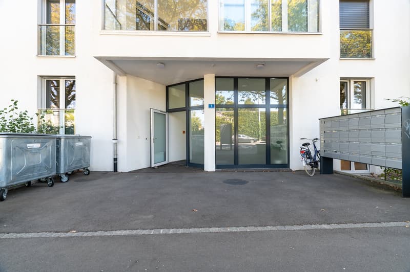 modern white building, large glass doors, arched entrance, several windows, bicycle parked, garbage bins