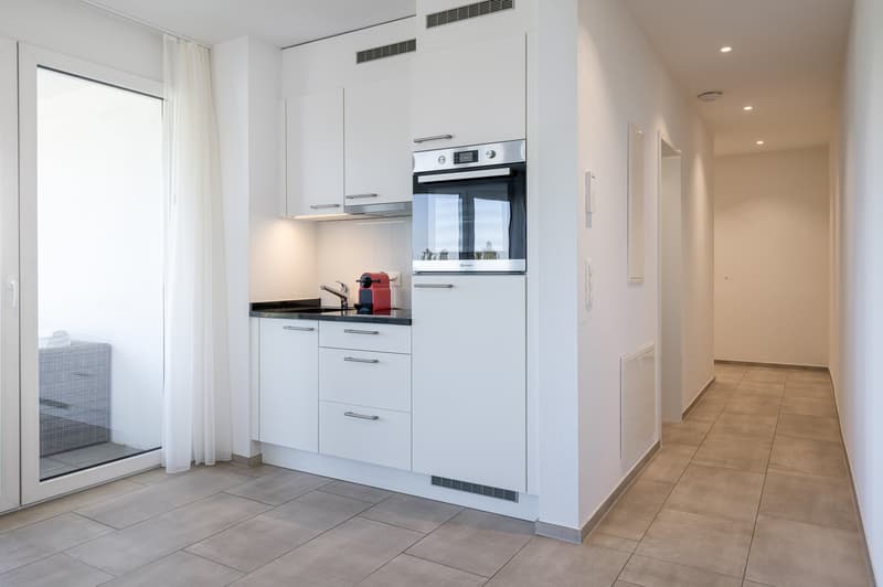 White kitchen with modern appliances, ceramic tiled floor, glass sliding door to terrace, faucet and kettle on countertop
