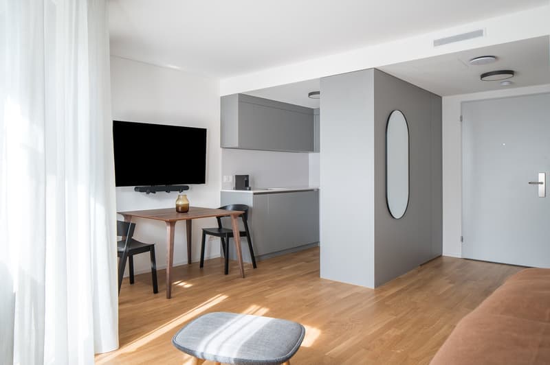 small room, wooden floor, table, chairs, TV mounted on wall, cabinets, microwave, counter, sink