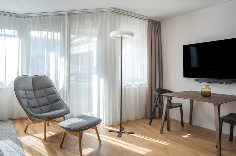 Wood floor, white curtains, modern light fixture, modern furniture, desk with vase, television
