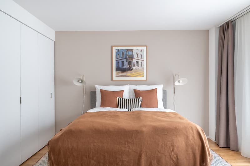 Double bed, white bedding, brown throw, bedside lamps, picture frame, curtains, wardrobe