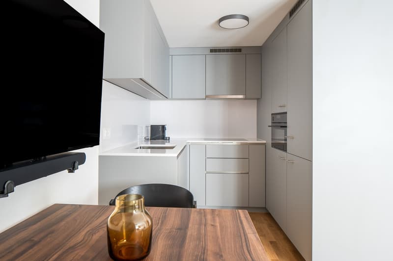 modern compact kitchen, wooden table, grey cabinets, black desk, flatscreen TV