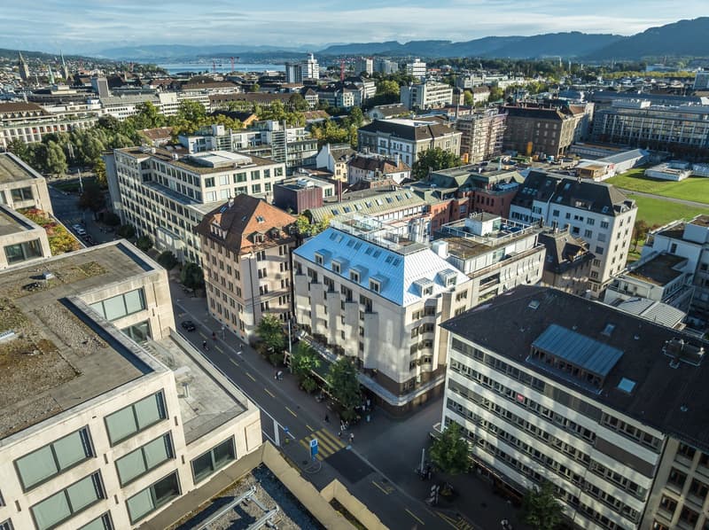 Aerial view of city, multiple buildings, various architecture styles, green spaces, roads, mountains in the distance